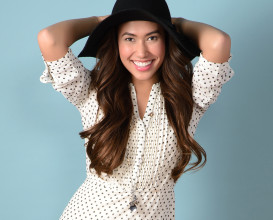 A girl smiling wearing a black and white polkadotted dress and black hat