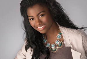 A girl smiling wearing a white jacket and colorful necklace