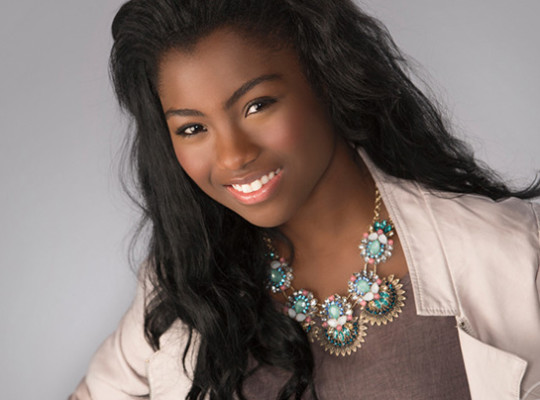 A girl smiling wearing a white jacket and colorful necklace