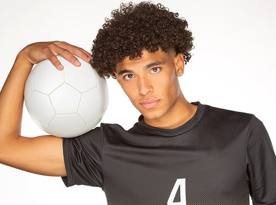 A guy wearing a black jersey holding a white soccer ball