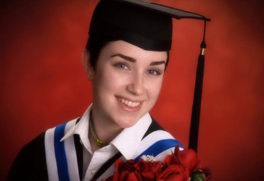Girl smiling wearing a graduation gown in front of red background
