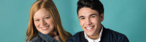 A girl and guy smiling in front of a teal background